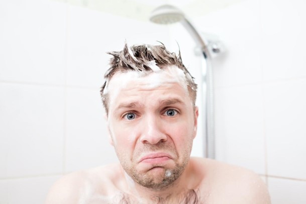 Guy in the shower with no hot water who needs to call Einstein Pros for water heater maintenance.